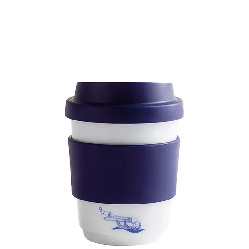 **Alt-Text:** Ein wiederverwendbarer Kaffeebecher aus Keramik in Weiß mit einem blauen Silikonring. Der Becher hat einen schmalen Deckel und zeigt eine Illustration eines Wals in einer verspielten, blauen Zeichnung. Die Kombination aus Weiß und Blau verleiht dem Becher ein modernes und frisches Design, ideal für umweltbewusste Kaffeetrinker.