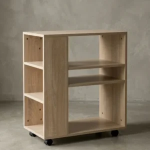 Freigestellter Rollwagen aus Holz in heller Eichenoptik von vorne. Das schmale Bücherregal (60cm breit) zeigt seine asymmetrischen Fächer und vier praktischen schwarzen Lenkrollen._#sku_BARWL5.695#